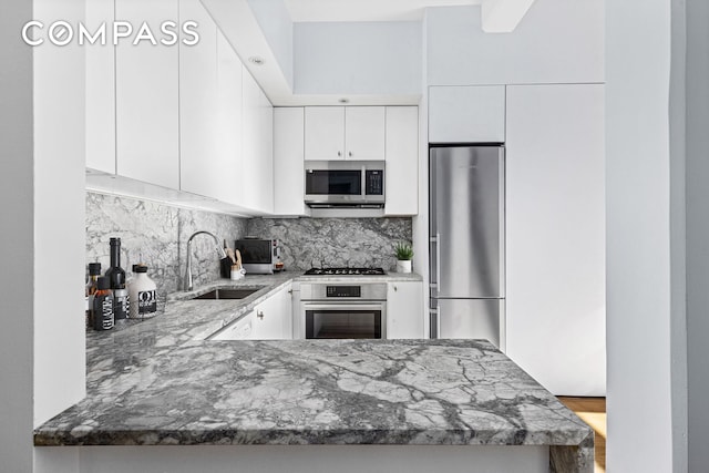 kitchen with light stone counters, stainless steel appliances, decorative backsplash, white cabinetry, and a sink