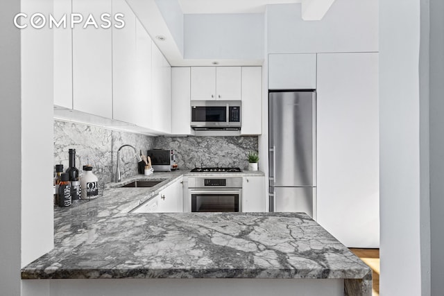 242 S 1st St Unit 4E, New York City, NY 11211 - kitchen featuring appliances with stainless steel finishes, a sink, backsplash, dark stone countertops, and white cabinetry