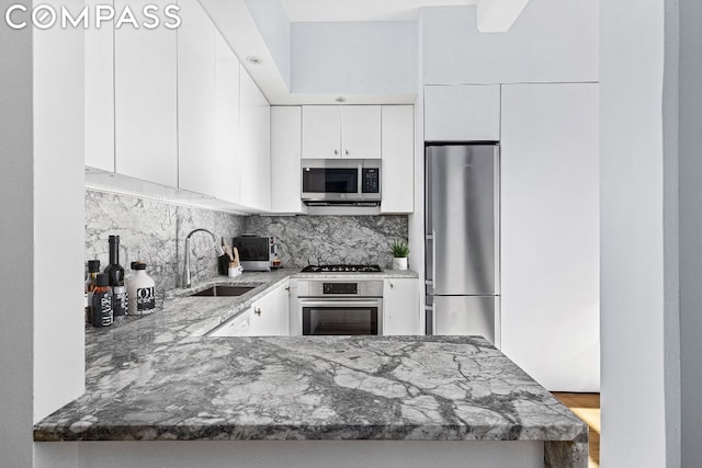 kitchen featuring white cabinetry, appliances with stainless steel finishes, decorative backsplash, light stone counters, and sink