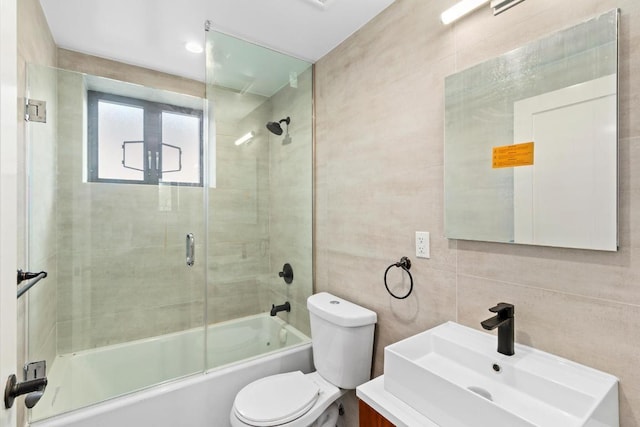 full bathroom featuring shower / bath combination with glass door, vanity, toilet, and tile walls