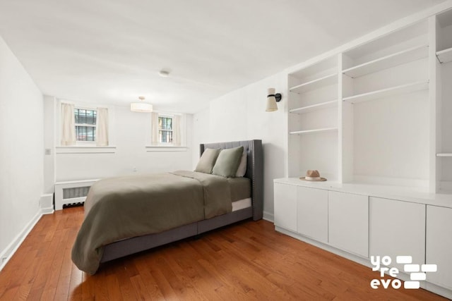 bedroom featuring light wood-type flooring, radiator heating unit, baseboards, and an AC wall unit