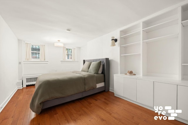 bedroom with an AC wall unit, baseboards, hardwood / wood-style floors, and radiator heating unit