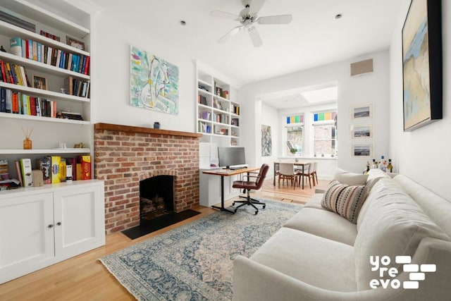 living area with light wood-type flooring, a brick fireplace, ceiling fan, and built in features