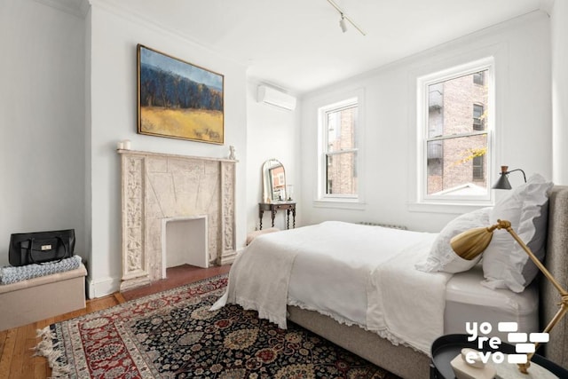 bedroom featuring ornamental molding, a wall mounted air conditioner, track lighting, and wood finished floors