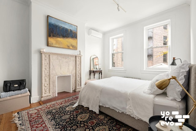 bedroom with ornamental molding, an AC wall unit, track lighting, and wood finished floors