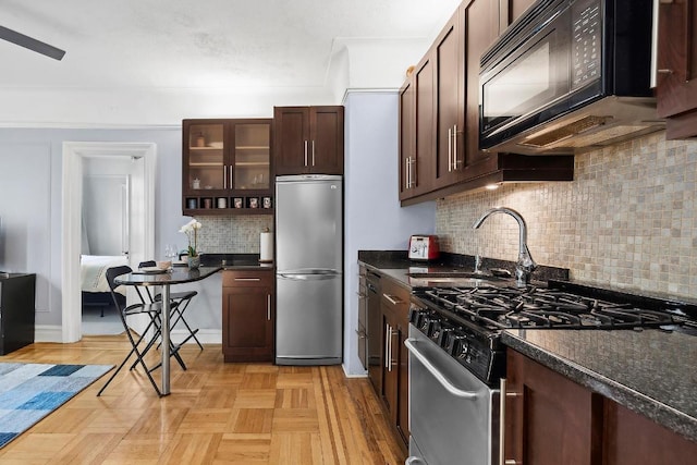 kitchen with light parquet floors, appliances with stainless steel finishes, dark stone countertops, dark brown cabinets, and decorative backsplash