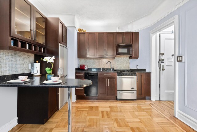 kitchen with dark countertops, a sink, black appliances, glass insert cabinets, and backsplash