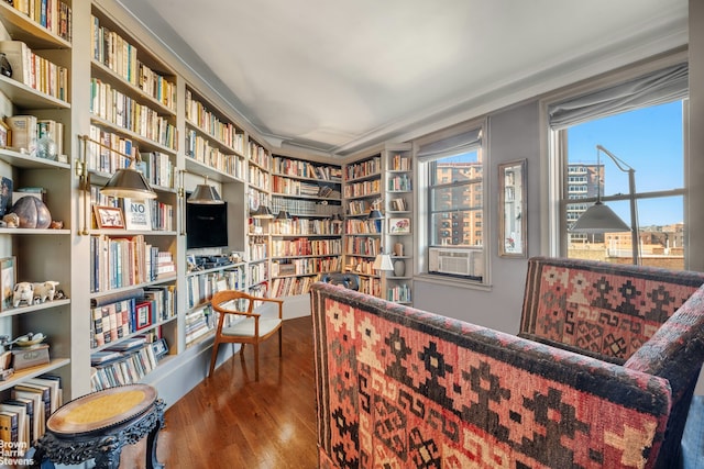 sitting room featuring cooling unit, bookshelves, and wood finished floors