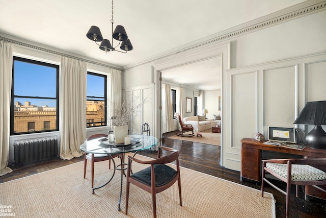 dining area featuring a decorative wall, radiator heating unit, ornamental molding, wood finished floors, and a notable chandelier