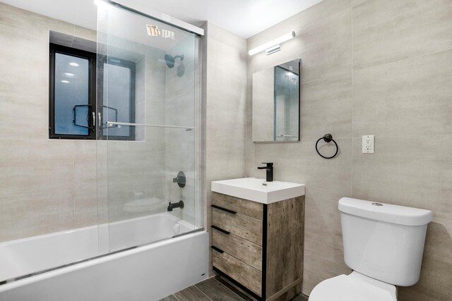 bathroom featuring toilet, enclosed tub / shower combo, tile walls, and vanity