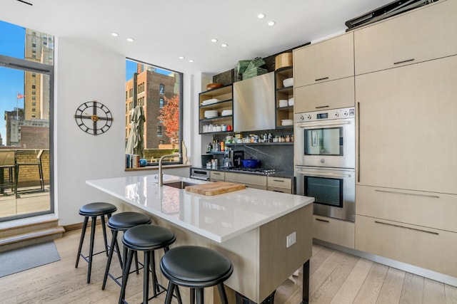 kitchen featuring a center island with sink, stainless steel double oven, sink, and a breakfast bar area