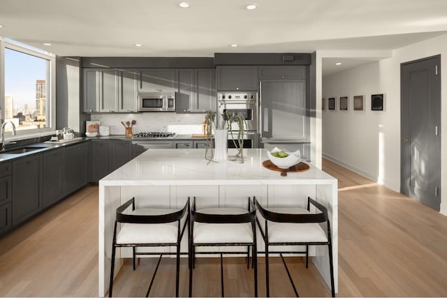 kitchen with appliances with stainless steel finishes, a kitchen breakfast bar, light stone counters, a center island, and a sink