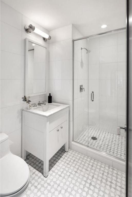 full bath with a stall shower, toilet, tile walls, and vanity