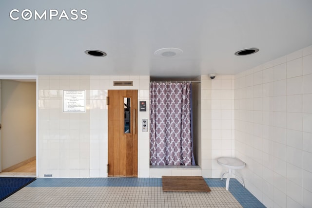 full bath featuring a shower with shower curtain, tile walls, visible vents, and tile patterned floors