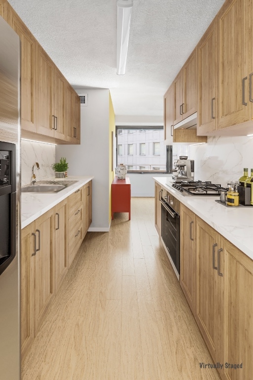 kitchen with stainless steel appliances, a sink, light wood finished floors, decorative backsplash, and a textured ceiling
