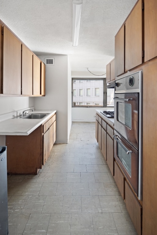 kitchen with visible vents, a sink, gas cooktop, stainless steel double oven, and light countertops