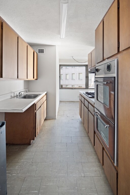 kitchen with double oven, a sink, light countertops, a textured ceiling, and gas stovetop