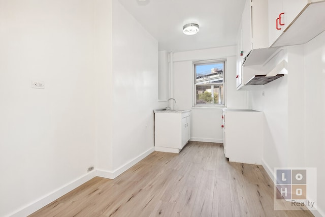 laundry area featuring laundry area, a sink, light wood-style flooring, and baseboards