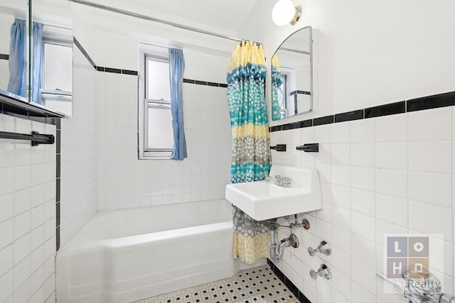 bathroom featuring tile walls, shower / bathtub combination with curtain, wainscoting, a sink, and tile patterned floors