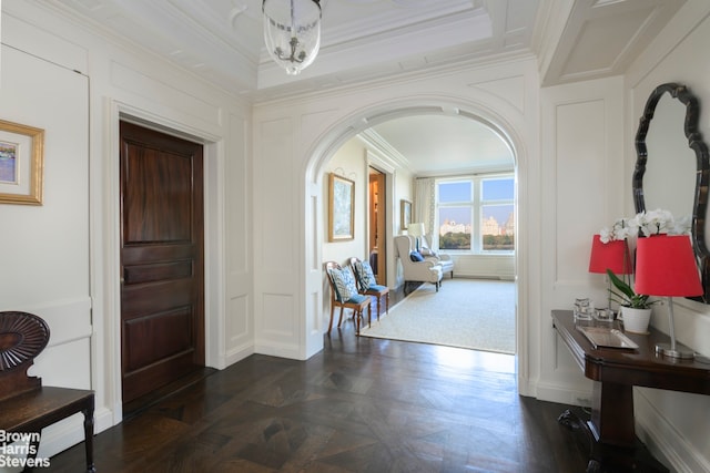 foyer entrance featuring a decorative wall, a notable chandelier, arched walkways, and ornamental molding