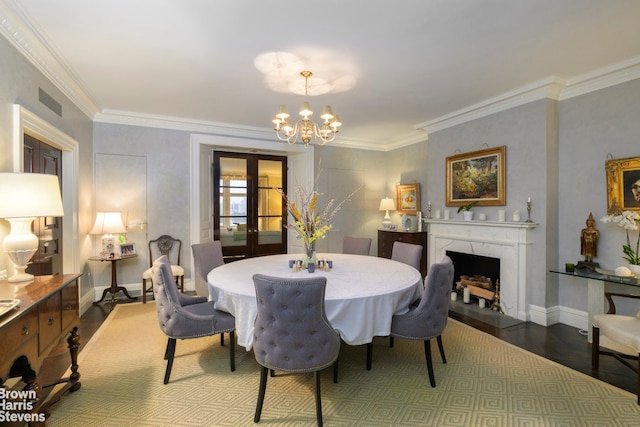 dining space featuring hardwood / wood-style floors, crown molding, a premium fireplace, an inviting chandelier, and french doors