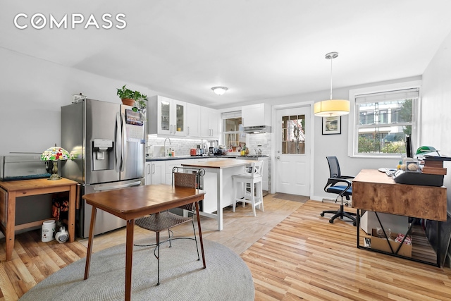 kitchen featuring stainless steel refrigerator with ice dispenser, tasteful backsplash, hanging light fixtures, glass insert cabinets, and white cabinets