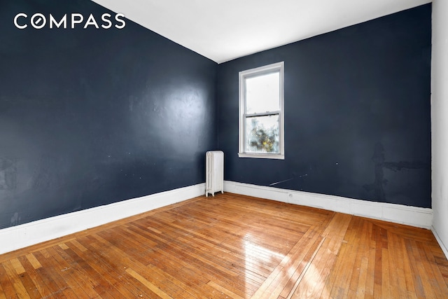 unfurnished room featuring radiator heating unit, baseboards, and wood-type flooring