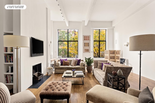 living area featuring a fireplace with flush hearth, beamed ceiling, and wood finished floors