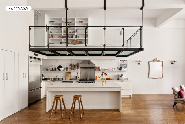 kitchen featuring stainless steel built in fridge, wall chimney exhaust hood, open shelves, and a sink