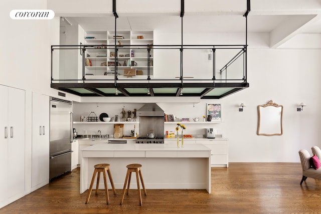 kitchen with open shelves, wall chimney exhaust hood, a kitchen island, and built in fridge