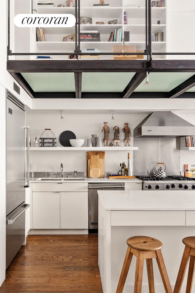 kitchen with dark wood-type flooring, wall chimney range hood, white cabinets, stainless steel appliances, and open shelves