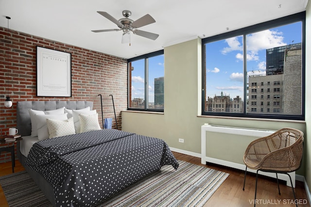 bedroom featuring wood finished floors, baseboards, brick wall, a view of city, and ceiling fan