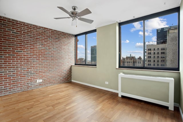 spare room with brick wall, a ceiling fan, a view of city, wood finished floors, and baseboards