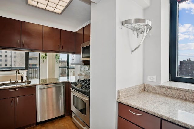 kitchen with appliances with stainless steel finishes, a sink, wood finished floors, tasteful backsplash, and light stone counters