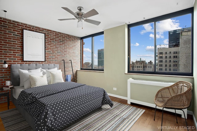 bedroom featuring a city view, wood finished floors, radiator, brick wall, and baseboards