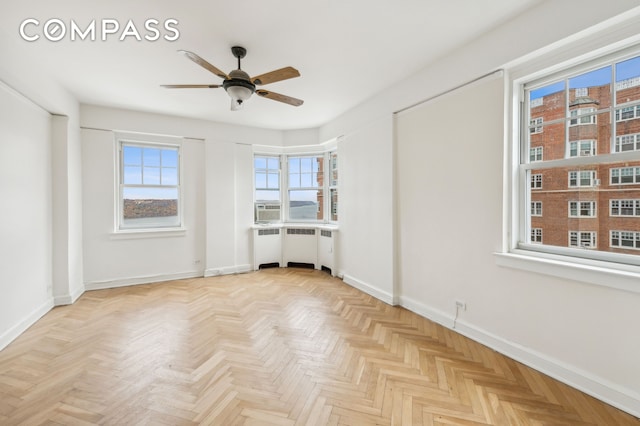 empty room featuring radiator heating unit, baseboards, and a ceiling fan