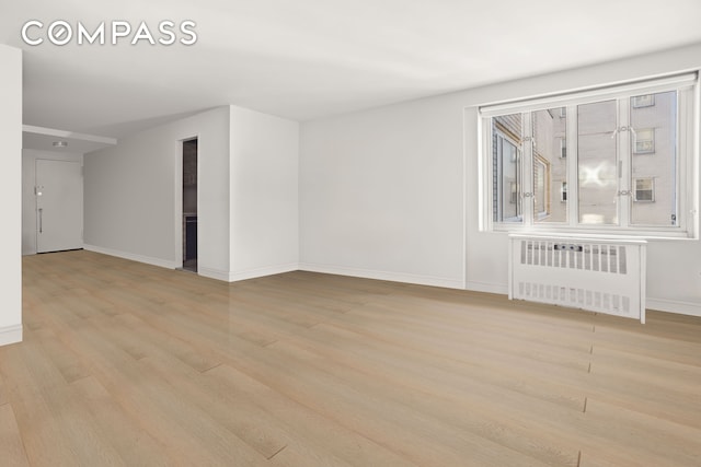 unfurnished room featuring baseboards, light wood-type flooring, and radiator