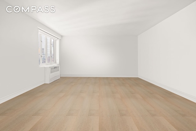 spare room featuring radiator, light wood-type flooring, and baseboards