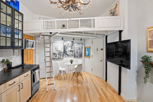 kitchen featuring stainless steel microwave, light wood-type flooring, electric range oven, decorative backsplash, and a notable chandelier