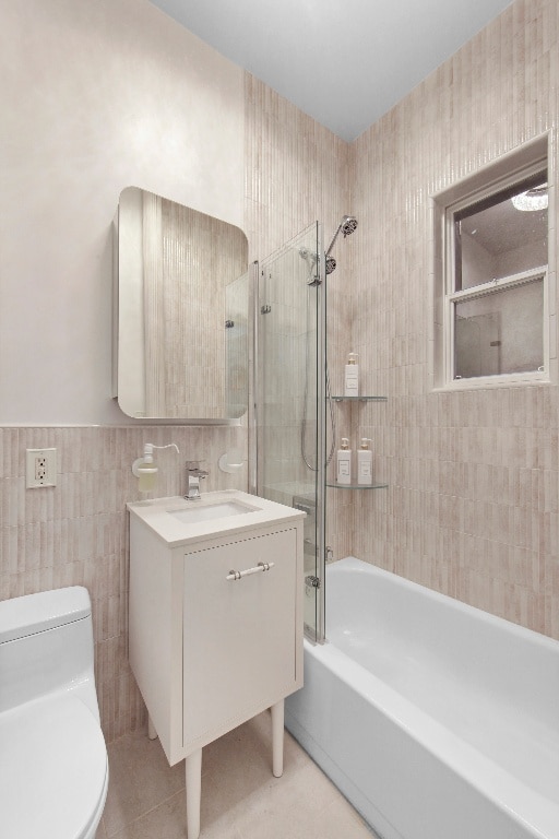 full bathroom featuring toilet, tile walls, vanity, tiled shower / bath combo, and tile patterned flooring