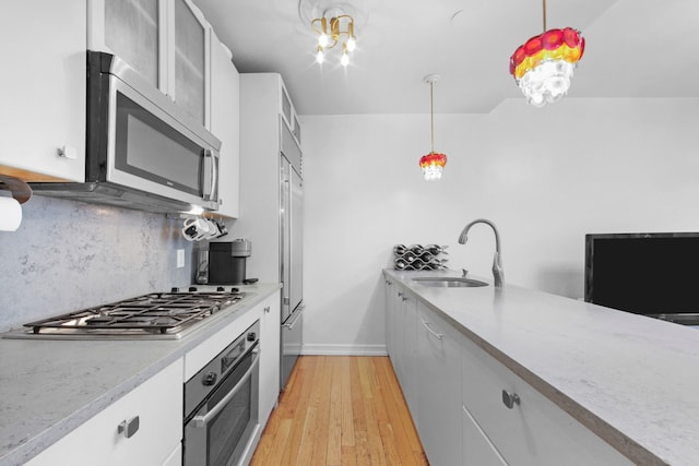 237 E 88th St Unit 101, New York City, NY 10128 - kitchen featuring stainless steel appliances, backsplash, decorative light fixtures, white cabinetry, and light wood finished floors