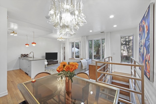 dining room with an inviting chandelier, sink, and light hardwood / wood-style flooring