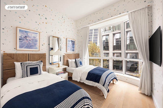 bedroom featuring visible vents, baseboards, wood finished floors, and wallpapered walls