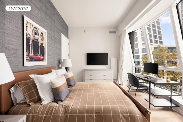 bedroom with an accent wall, wood finished floors, visible vents, and wallpapered walls