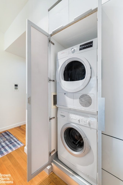 laundry room featuring stacked washer and clothes dryer and light hardwood / wood-style flooring