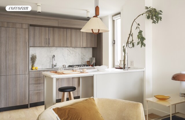 kitchen with decorative light fixtures, tasteful backsplash, sink, kitchen peninsula, and light wood-type flooring