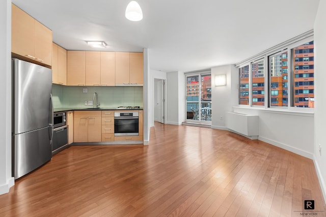 kitchen featuring dark countertops, decorative backsplash, light brown cabinetry, appliances with stainless steel finishes, and a sink