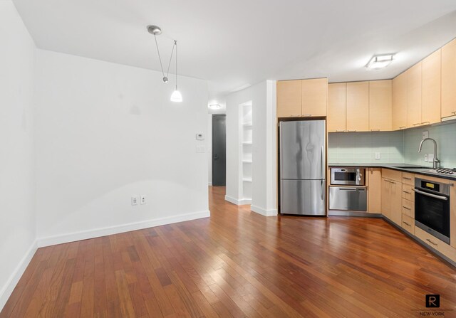 kitchen with stainless steel appliances, hardwood / wood-style flooring, sink, and backsplash