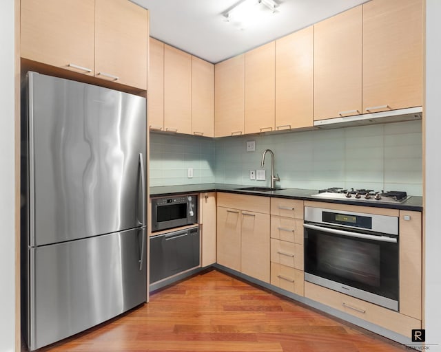 kitchen with a sink, cream cabinetry, under cabinet range hood, appliances with stainless steel finishes, and dark countertops