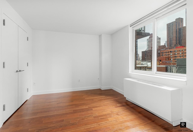 unfurnished bedroom featuring baseboards, a view of city, and light wood finished floors